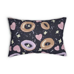 Puede incluir: Una almohada negra con un patrón repetido de corazones rosas, estrellas amarillas y donuts coloridos. Los donuts están glaseados y tienen chispas.