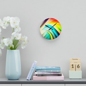 May include: A colorful abstract clock with a rainbow design. The clock is round and has a white background with a black clock face. The clock is hanging on a white wall.