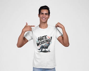 Puede incluir: Camiseta blanca con el texto "HATE WORKING!" en una fuente audaz y estilizada. El gráfico presenta a una persona relajándose en una silla de oficina. La persona de la imagen señala la camiseta.