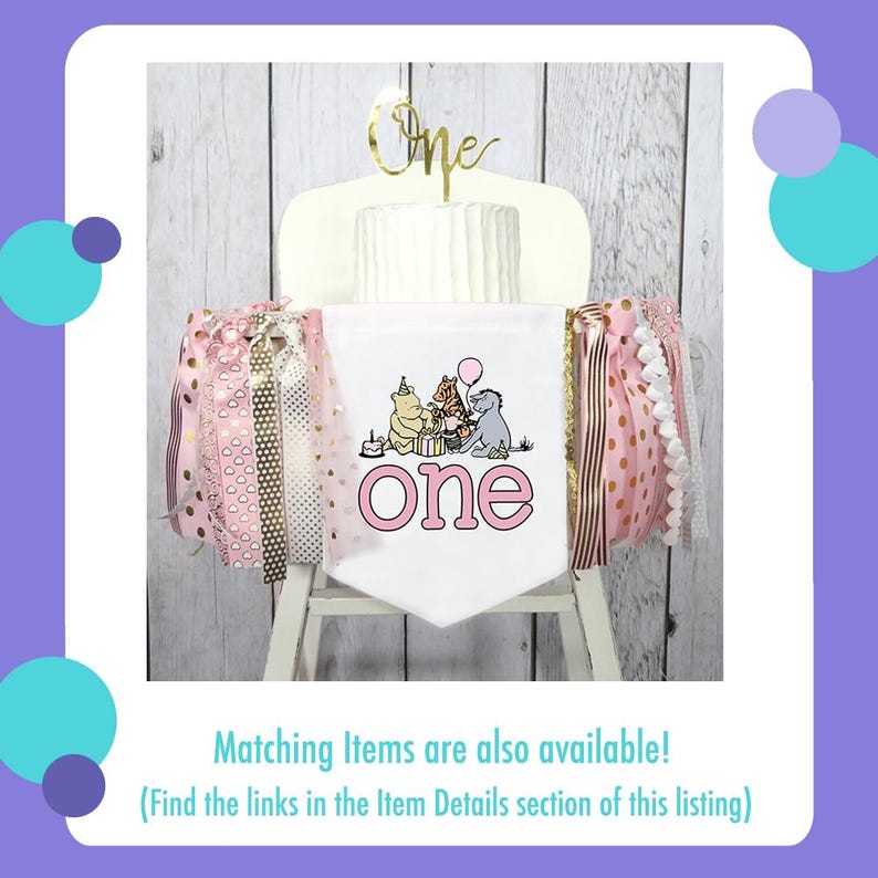 Puede incluir: Una tarta blanca con un adorno dorado de "One", decorada con una pancarta con los personajes de Winnie the Pooh y la palabra "one" en rosa. Cintas rosas y doradas adornan los lados, creando un aspecto festivo.