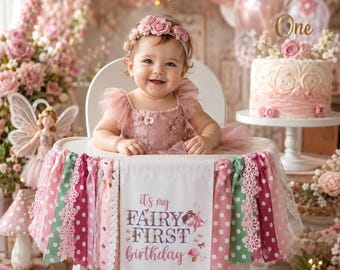May include: A high chair banner featuring a white fabric pennant with the text 'it's my FAIRY FIRST birthday' and a fairy illustration, surrounded by hanging ribbons in shades of pink, green, and white with polka dot and lace patterns.