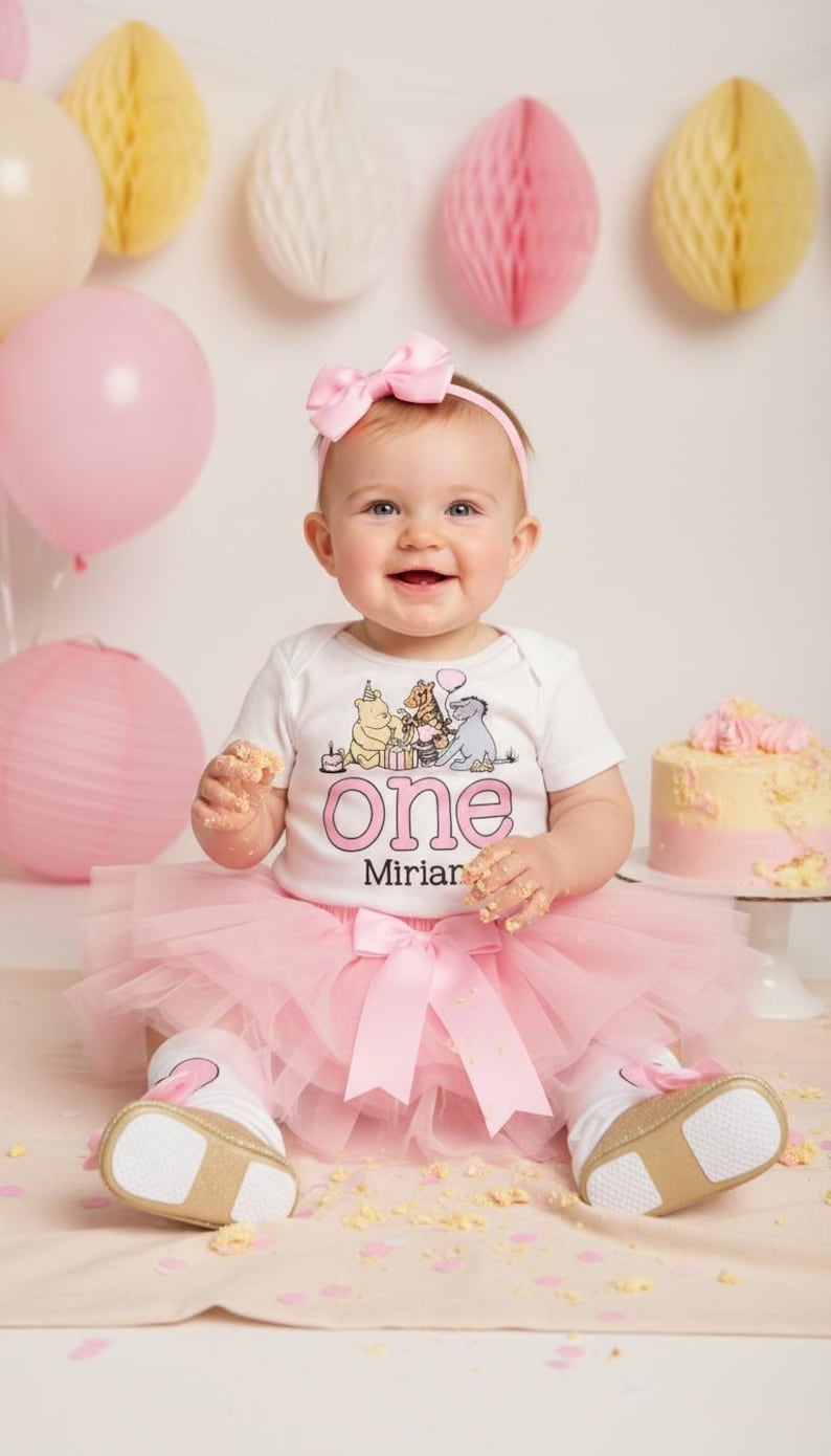 Puede incluir: Un beb&eacute; con un body blanco con un dise&ntilde;o de Winnie the Pooh y la palabra "One" en rosa, combinado con un tut&uacute; y un lazo rosa. El beb&eacute; sonr&iacute;e, rodeado de globos rosas, decoraciones de papel y una tarta.