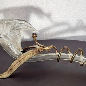 May include: A clear glass flower-shaped sculpture with a curved stem and a spiral design. The sculpture has gold-colored accents and is likely a decorative piece for the home.