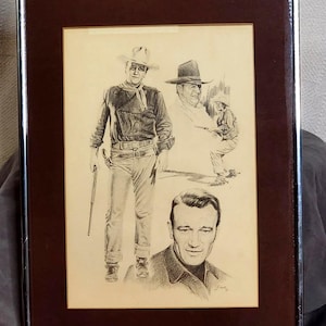 Puede incluir: Un boceto a lápiz en blanco y negro enmarcado que presenta tres representaciones de John Wayne. La figura central viste ropa de vaquero con sombrero y rifle, mientras que una versión más pequeña y un retrato en primer plano aparecen.