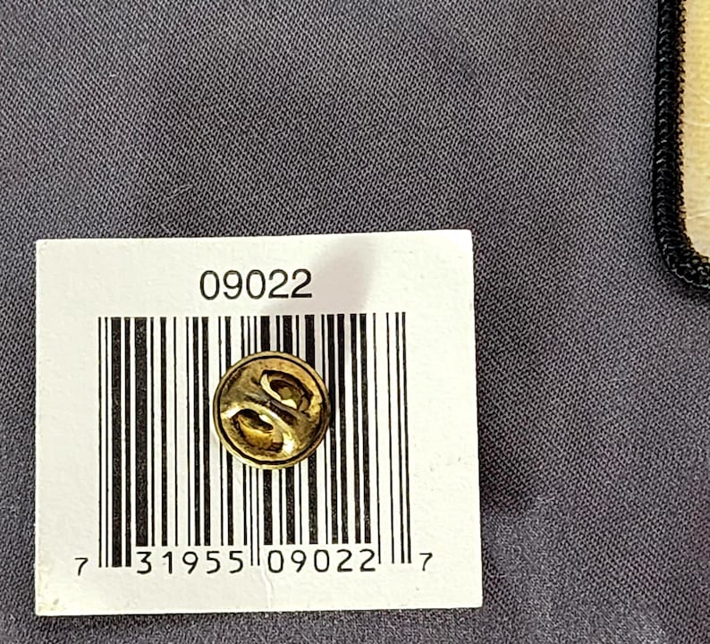 May include: A gold-colored lapel pin with a decorative design. The pin is round and has a butterfly clutch back. The image also shows a white label with the number "09022" and a barcode.