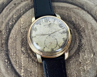May include: A vintage wristwatch with a gold-tone round case and a black leather strap. The off-white dial features the text DOYLE 17 RUBIS and ANTIMAGNETIC, with a small sub-dial at the bottom, gold-tone hands, and black numeral hour markers.