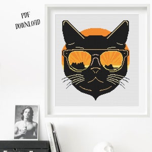 May include: Cross-stitch artwork of a black cat wearing sunglasses, set against an orange sunset. The design is framed in a white square frame. Text in the upper left corner reads "PDF DOWNLOAD".