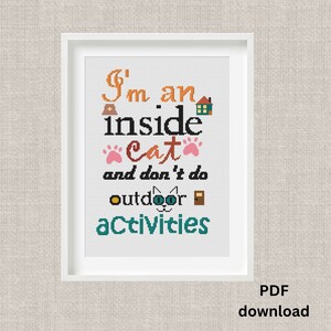 Può includere: Opera d'arte a punto croce incorniciata con la scritta "I'm an inside cat and don't do outdoor activities." Il testo è in vari colori, tra cui arancione, nero, rosa, giallo e verde acqua. L'opera è in una cornice bianca.