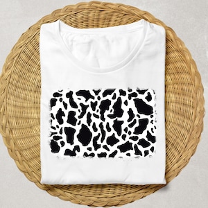 Może przedstawiać: Biała koszulka z czarno-białym wzorem krowiej skóry.
