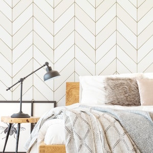 Op de afbeelding: Een slaapkamer met een wit bed met een grijs en wit deken en een wit hoofdeinde. De muur achter het bed heeft een wit en gouden chevron-patroon behang.