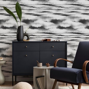 May include: A living room interior with a black and white patterned wallpaper, a dark blue armchair, a dark blue dresser with gold handles, a white side table, a white fluffy pouf, and a beige rug.