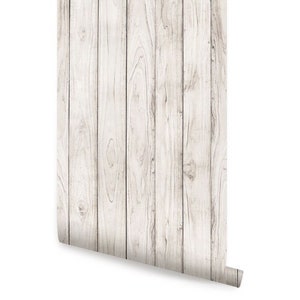 May include: White woodgrain wallpaper with a vertical plank pattern. The wallpaper is rolled up and ready to be applied to a wall.
