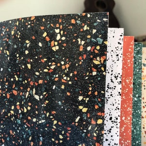 Può includere: Un set di sei fogli di carta con motivi diversi con un design in terrazzo. I motivi presentano vari colori, tra cui nero, bianco, rosso, giallo e verde.