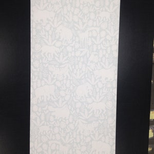 Puede incluir: Un rollo de papel pintado con un fondo azul claro y un diseño de jungla blanco. El patrón incluye elefantes, tigres, jirafas y plantas tropicales. El papel pintado está listo para ser aplicado.