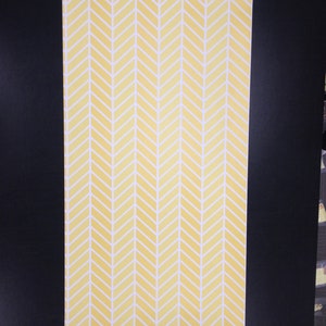 May include: A yellow and white chevron pattern wallpaper roll. The pattern is a repeating chevron design with a subtle watercolor effect.