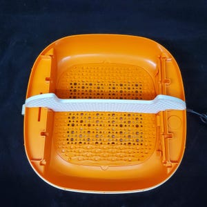 May include: Orange and white plastic foot spa with a gridded bottom and a white divider. The spa has a cord for plugging in.