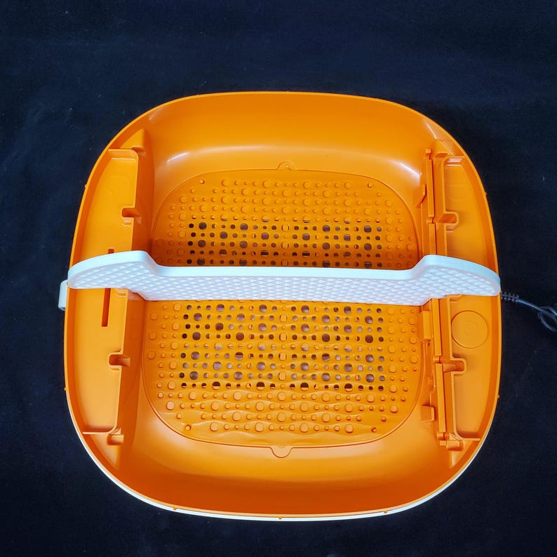May include: Orange and white plastic foot spa with a gridded bottom and a white divider. The spa has a cord for plugging in.