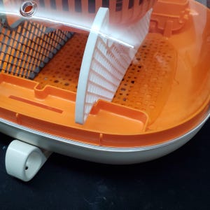 May include: Orange and white plastic baby bottle drying rack with a clear plastic lid. The rack has a gridded base and a removable tray.