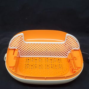 May include: An orange and white plastic foot bath with a white mesh insert. The foot bath has a textured bottom and a white lid.