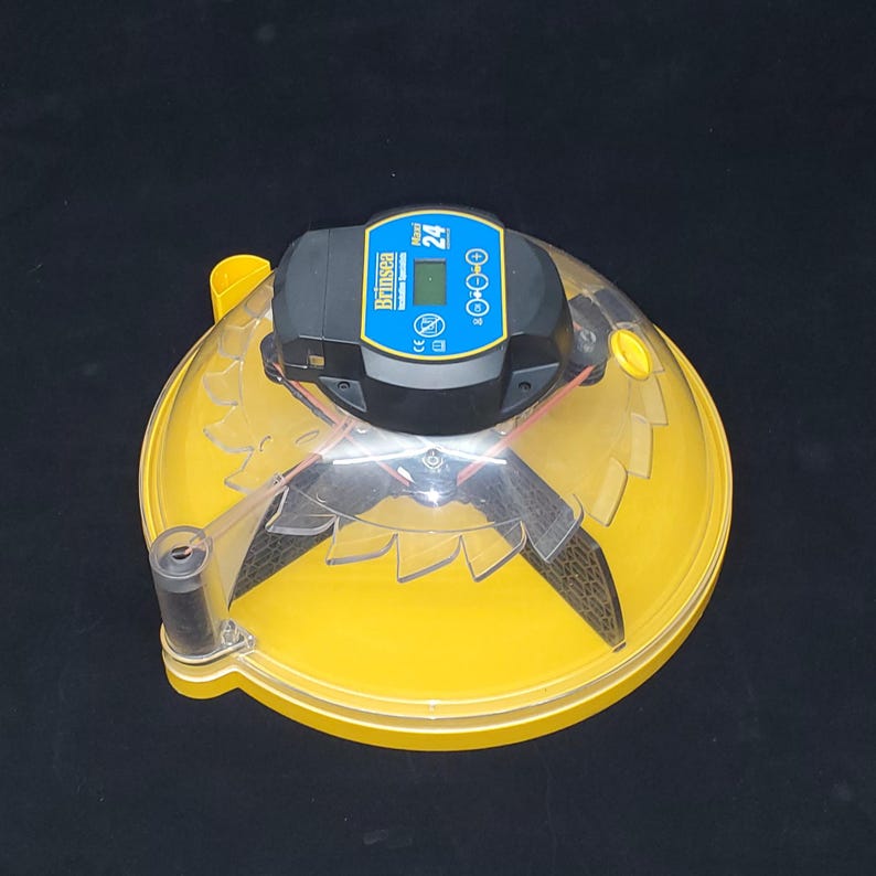 Puede incluir: Un volteador de huevos autom&aacute;tico amarillo con una c&uacute;pula de pl&aacute;stico transparente y una pantalla digital negra que muestra "Brinsea 24".