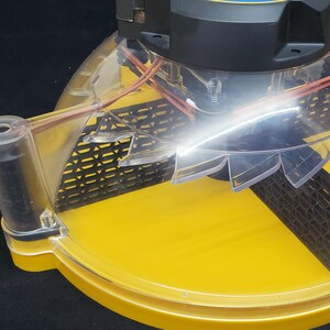 Puede incluir: Primer plano de un ventilador amarillo y negro con aspas de pl&aacute;stico transparente y una rejilla de malla de alambre negro. El ventilador es parte de un dispositivo m&aacute;s grande, posiblemente un sistema de refrigeraci&oacute;n.