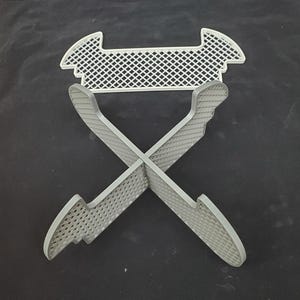 May include: A white plastic stand with a grid pattern. The stand is designed to hold items upright and has four legs that form an X shape. The stand is made of a lightweight material and is easy to assemble.