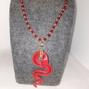 Red and gold glass snake pendant with red and gold beads on golden chain.