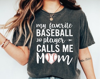 May include: A dark gray t-shirt with the text "my favorite baseball player calls me mom" in white with a red and white baseball graphic inside a heart.