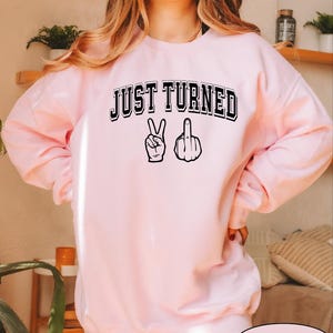 a woman wearing a pink sweatshirt that says just turned up