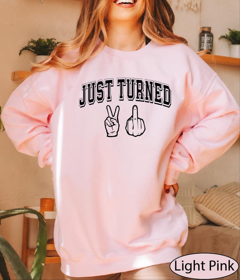 a woman wearing a pink sweatshirt that says just turned up