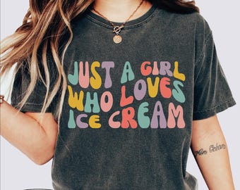 Könnte beinhalten: Dunkelgraues T-Shirt mit dem Text "JUST A GIRL WHO LOVES ICE CREAM" in bunten Buchstaben im Retro-Stil. Das Shirt hat einen Vintage-Look.