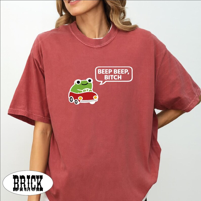 A woman wearing a red t-shirt with a cartoon frog and the text "BEEP BEEP, BITCH" printed on it.