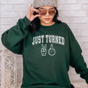 a woman wearing a green sweatshirt that says just turned