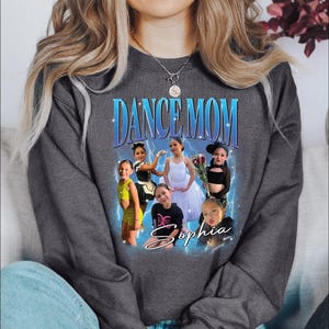 a woman sitting on a couch wearing a dance mom sweatshirt