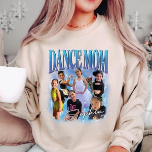 a woman sitting on a couch wearing a dance mom sweatshirt