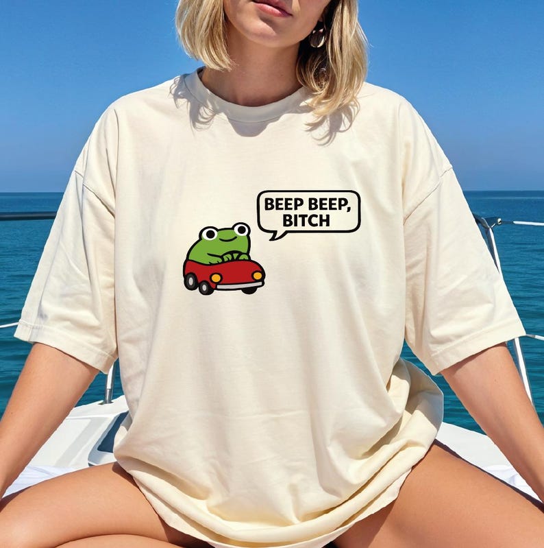 A person wearing a white t-shirt with a cartoon frog and text that says "BEEP BEEP BITCH" against a blue background.