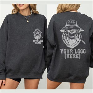 May include: Charcoal gray sweatshirt with a white graphic of a gorilla wearing a hat and holding a cigar. The text "YOUR LOGO (HERE)" is below the graphic on the front and back. The sweatshirt is a crew neck style.