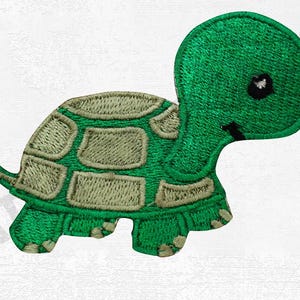 May include: Embroidered patch of a green turtle with a light green shell pattern. The turtle has a smiling face with a black eye and a small black mouth. The patch is designed for application on clothing or accessories.
