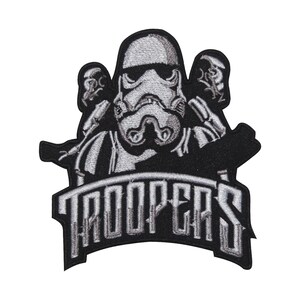 Könnte beinhalten: Gestickter Aufnäher mit drei Stormtrooper-Figuren in Schwarz-Weiß. Das Wort "TROOPERS" wird in einer stilisierten Schriftart angezeigt. Der Aufnäher hat einen schwarzen Rand und ist für das Aufnähen auf Kleidung oder Accessoires konzipiert.