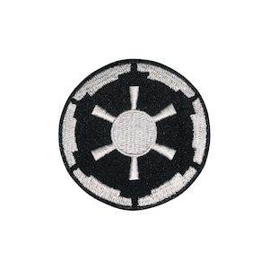Op de afbeelding: Een ronde zwarte patch met een wit Imperial symbool. Het symbool bestaat uit een centrale cirkel met zes spaken en een gesegmenteerde rand. Geschikt voor kleding of accessoires.