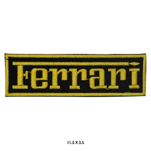 May include: Embroidered patch with the word "Ferrari" in yellow on a black background. The rectangular patch measures 29.2 cm by 8.9 cm. The text is in a bold, sans-serif font, and the border is yellow.