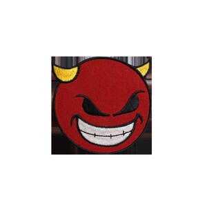 Puede incluir: Un parche bordado rojo con la cara de un diablo, cuernos amarillos, ojos negros y una boca sonriente con dientes blancos. El parche es circular y está sobre un fondo negro.