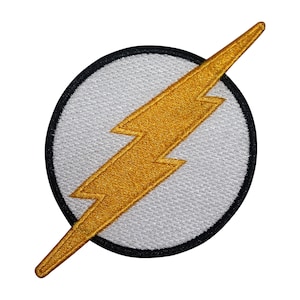 May include: Embroidered patch with a gold lightning bolt on a white circle, edged in black. The lightning bolt is angled across the circle. The patch is designed for application on clothing or accessories.