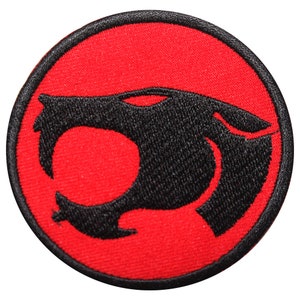 Może przedstawiać: Okrągła, haftowana naszywka z czarną sylwetką głowy pantery na czerwonym tle. Naszywka ma czarną obwódkę. Projekt jest stylizowaną reprezentacją dużego kota.