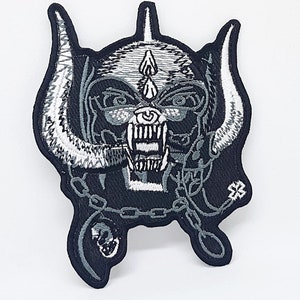 May include: Embroidered patch depicting a skull with horns, fangs, and a chain, in black, white, and grey. The patch has detailed stitching and a heavy metal design, ideal for application on clothing or accessories.