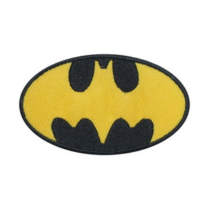 May include: An oval-shaped embroidered patch featuring the Batman logo. The patch has a yellow background with a black bat symbol in the centre, outlined with black stitching.