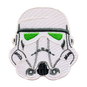 May include: Embroidered patch featuring the iconic helmet of a Stormtrooper from Star Wars. The patch is primarily white with black and green accents, including the visor and details of the helmet. The design is detailed and suitable for application on clothing or accessories.