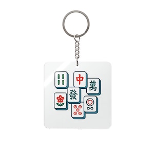 May include: A white square keychain with a selection of colourful Mahjong tiles. The tiles display various symbols and characters in red, green, and blue. The keychain has a silver ring and chain.