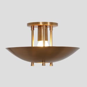 May include: A brass ceiling light fixture with a wide, shallow bowl shape and a central light bulb. The fixture has four decorative accents on the bottom of the bowl and four vertical supports around the light bulb.