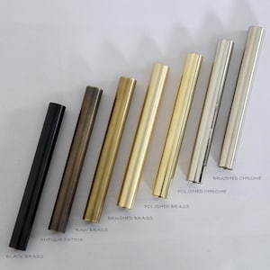K&ouml;nnte beinhalten: Nahaufnahme von acht Metallst&auml;ben in verschiedenen Ausf&uuml;hrungen, darunter Schwarzmessing, Antik-Patina, Rohmessing, geb&uuml;rstetes Messing, poliertes Messing, poliertes Chrom und geb&uuml;rstetes Chrom. Die St&auml;be sind von links nach rechts in einer Reihe angeordnet, wobei die dunkelste Ausf&uuml;hrung links und die hellste Ausf&uuml;hrung rechts ist.